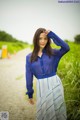 A woman in a blue shirt and white skirt standing on a dirt road.