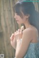 A woman in a blue dress standing in front of a wooden fence.