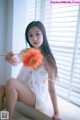 A woman sitting on a window sill holding a flower.