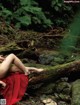 A woman in a red dress sitting on a log in the woods.