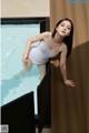 A woman in a white tank top leaning against a wall next to a pool.